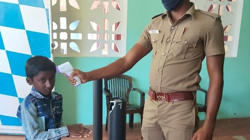 Ein Polizist misst die Temperatur eines Kindes vor der Übergabe des Patenschaftsgelds.