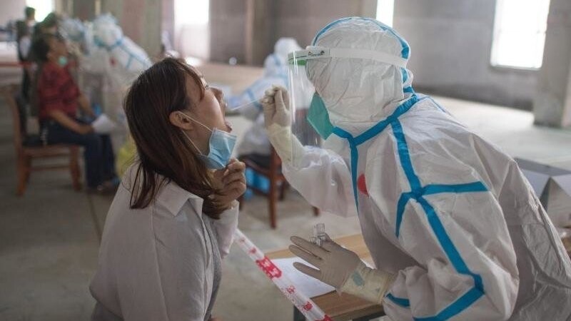 Eine Frau wird in Wuhan von einer Person in Schutzanzug auf das Coronavirus getestet. Wissenschaftler haben in der chinesischen Metropole Freiwilligen den Wirkstoff Ad5-nCoV verabreicht und berichten von ersten Erfolgen.