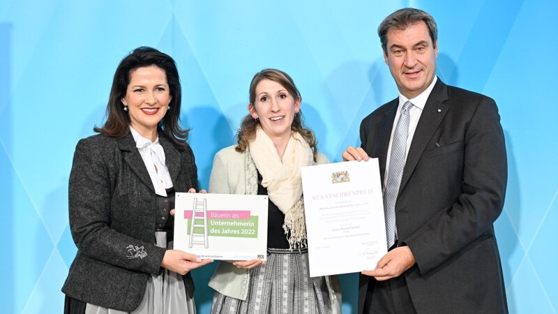 Die Bayerische Agrarministerin Michaela Kaniber (links) und Ministerpräsident Markus Söder (rechs) überreichen Lena-Maria Fischer (Mitte) den Staatsehrenpreis.