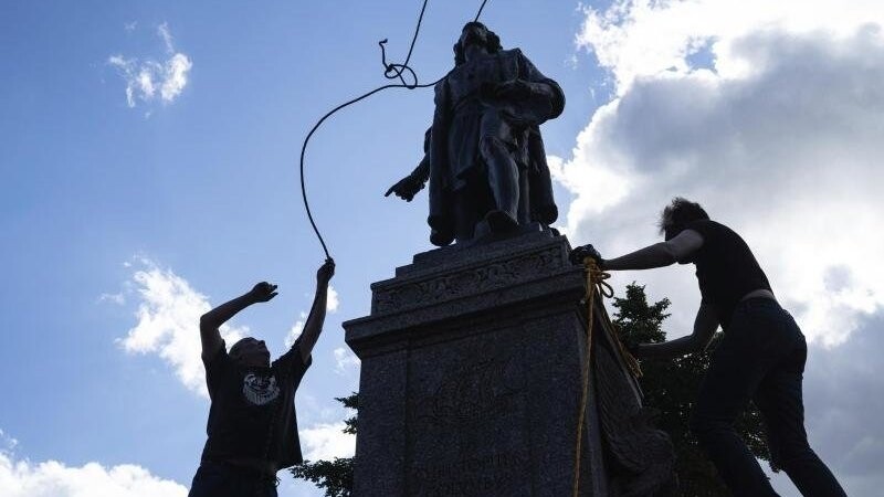 Zwei Männer befestigen ein Seil um den Hals einer Statue von Christopher Columbus.