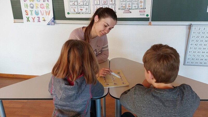 Alina Demeshko schlüpft in die Rolle der Lehrerin. In ihrer Hand hält sie einen Hörstift. Die beiden Kinder sind dabei, Deutsch zu lernen.