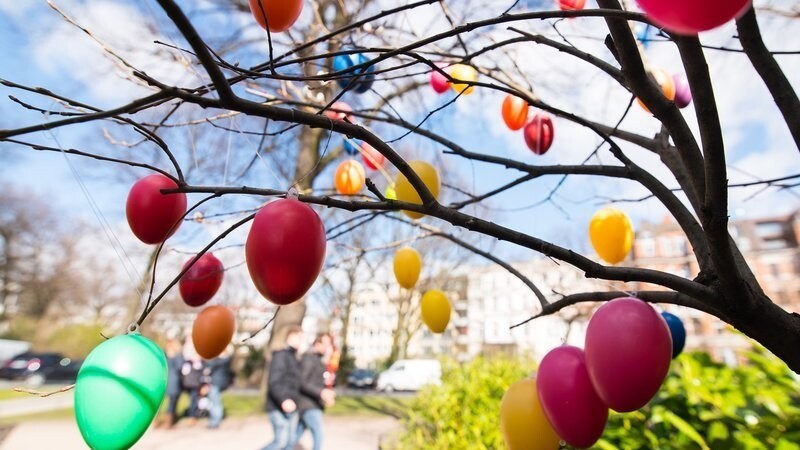 Spaziergänger gehen am 03.04.2015 in Hamburg an der Außenalster an einem Baum mit Ostereiern vorbei. Auch wenn es sich derzeit kaum danach anfühlt - an Ostern könnte es in Deutschland richtig warm werden.