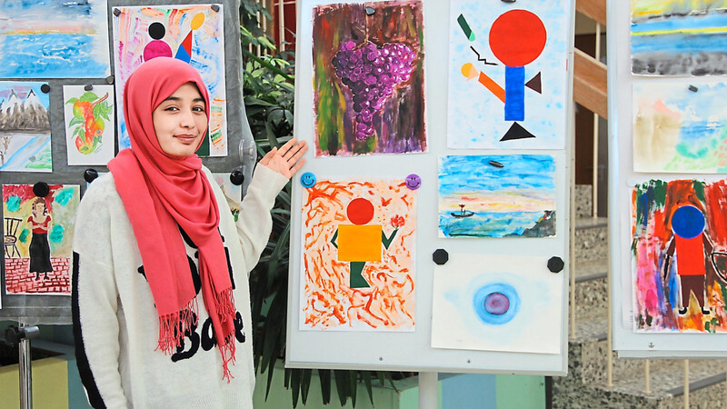 Zahra vor ihren Bildern. Von einem Zeichenlehrer inspiriert hat sie gelernt, Figuren aus geometrischen Formen zu entwickeln und gezielt Farbe einzusetzen.