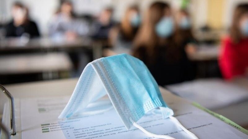 Eine Maske liegt im Unterricht an einem Gymnasium in München auf Schulunterlagen.