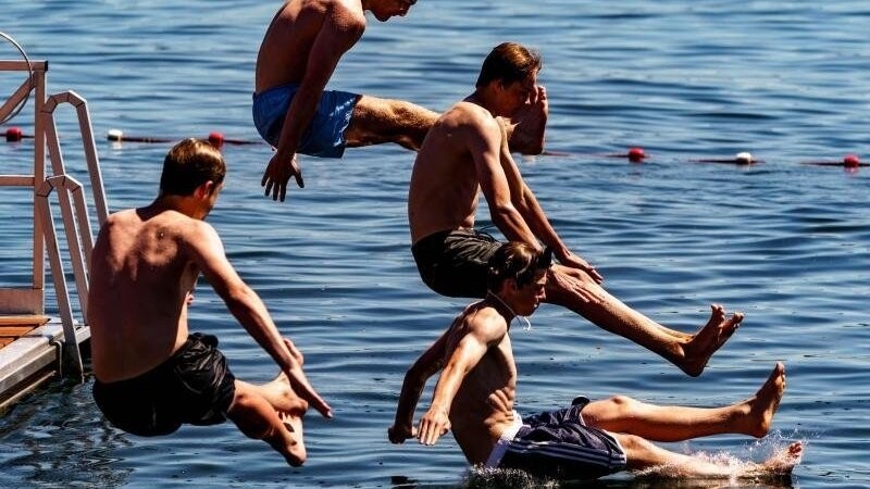 Vier junge Männer springen von einer Schwimmplattform aus in die Kieler Förde. Auch im Norden startet der Sommer mit großer Hitze durch.