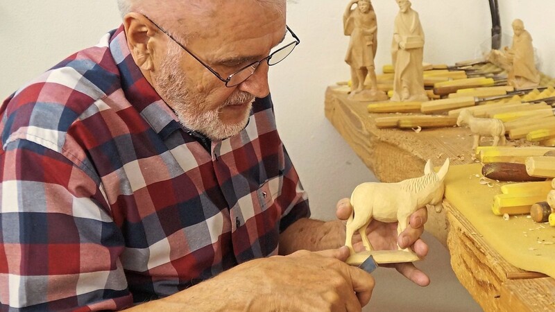 Konzentriert schnitzt Reinhold Andreas in der hauseigenen Werkstatt mit einem seiner rund 200 Schnitzmesser an einem kleinen Esel aus Holz. Voller Akribie widmet er sich dabei den Details der Krippenfigur.