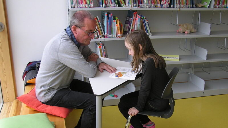Ein Lesepate übt mit einer Grundschülerin das Lesen.