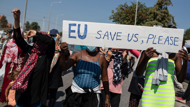 Migrantinnen und Migranten rufen bei einem Protest vor rund zwei Wochen auf Lesbos Parolen und halten ein Schild mit der Aufschrift "EU, save us, please" (EU, rette uns bitte).