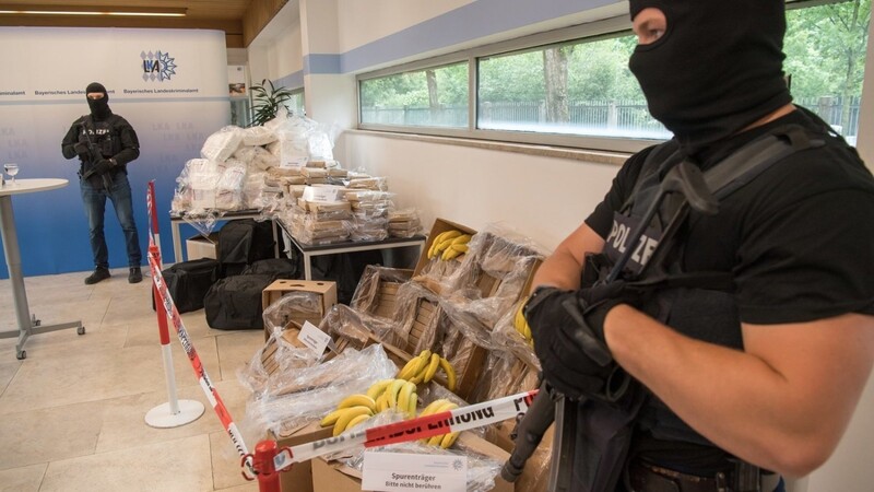 Schwer bewaffnete und vermummte Polizeibeamte bewachen während einer Pressekonferenz im bayerischen Landeskriminalamt etwa 640 Kilo Kokain, Waffen, Bargeld, Bananen sowie Bananenkisten.