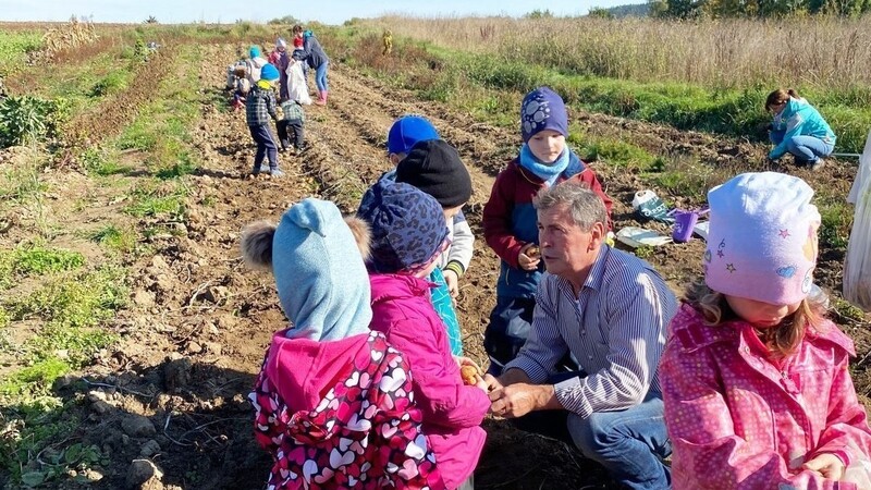 Inmitten der Kindergarten-Kinderschar sitzt Feldbetreuer Josef Auburger. Er erklärt den Kindern, was es mit dem Kartoffelanpflanzen auf sich hat.