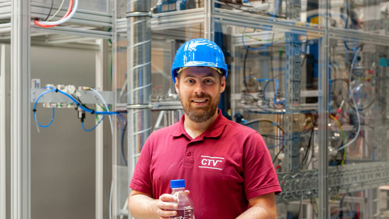 Jakob Burger, Professor für Chemische und Thermische Verfahrenstechnik, vor seiner Demonstrationsanlage am TUM-Campus Straubing. Die Flasche enthält auf dieser Anlage hergestelltes Oxymethylenether (OME).