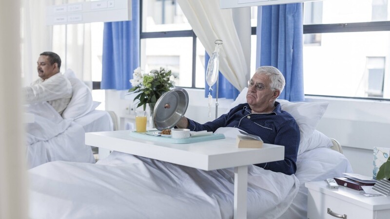 Skeptisch beäugt dieser Patient das, was sich unter der Warmhaltehaube verbirgt. Am Essen in Krankenhäusern, auch in München, wird oft gespart.
