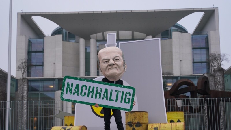 Ein als Bundeskanzler Scholz verkleideter Aktivist steht bei einer Demonstration Mitte Januar mit einem Transparent mit der Aufschrift "Nachhaltig" vor einem nachgebildeten Atomkraftwerk am Bundeskanzleramt.