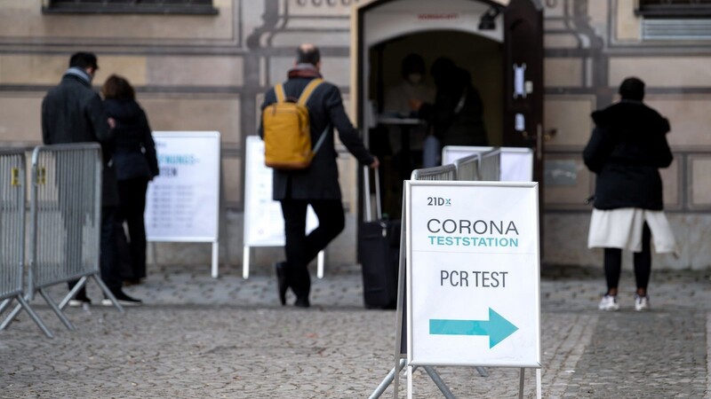 Menschen stehen vor einer Corona-Teststation in der Innenstadt in einer Warteschlange. Die Virusvariante Omikron treibt die Corona-Zahlen in Bayern weiter nach oben.