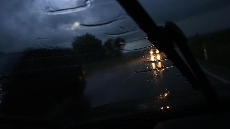 Hinter einem Scheibenwischer fahren Autos im Starkregen auf einer Straße (Symbolbild).