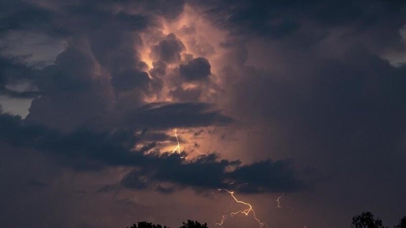 Ein Blitz hellt hinter dunklen Wolken auf.