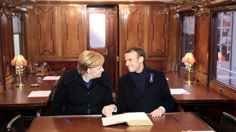 Bundeskanzlerin Angela Merkel und Frankreichs Präsident Emmanuel tragen sich in das Goldene Buch des Museums der Gedenkstätte bei Compiègne ein. Sie sitzen in einem Eisenbahnwaggon, der den Waggon von 1918 symbolisieren soll, in dem der Waffenstillstand geschlossen wurde.