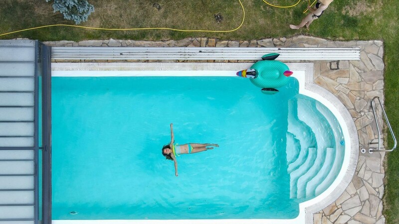 Ein Kind schwimmt in einem Pool, während ein anderes Mädchen den Rasen mit einem Wasserschlauch beregnet. In Berg in der Oberpfalz wird das Trinkwasser knapp. Deswegen müssen viele wohl erst einmal auf ihren Pool verzichten (Symbolbild)