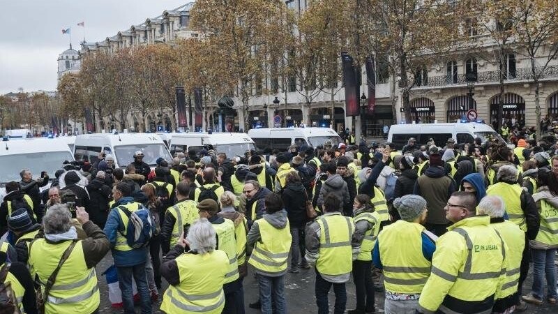 Demonstranten in gelben Warnwesten treffen auf den Champs-Élysées auf eine Polizeisperre.