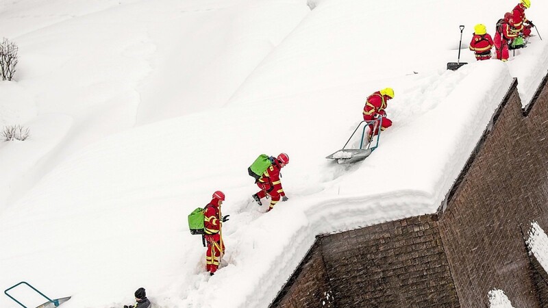 Helfer der Deutschen Lebens-Rettungs-Gesellschaft (DLRG) räumen im Landkreis Traunstein mit sogenannten Schneehexen Schnee von einem Hausdach.