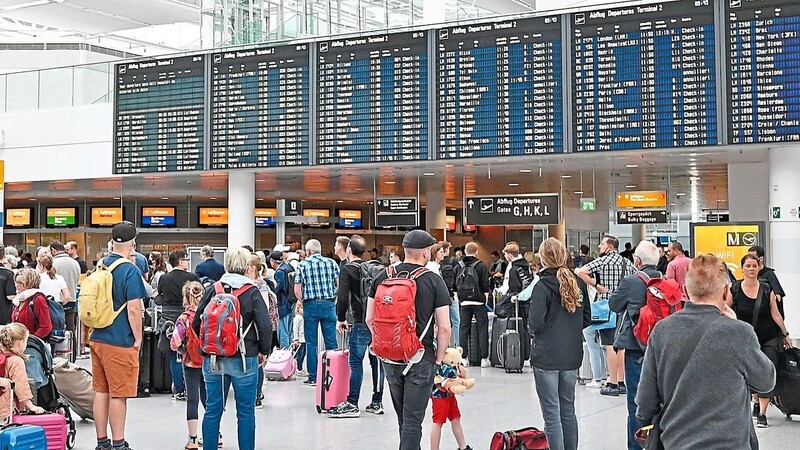 Flugreisende die im Terminal 2 am Flughafen München laufend die Anzeigetafel im Blick haben.