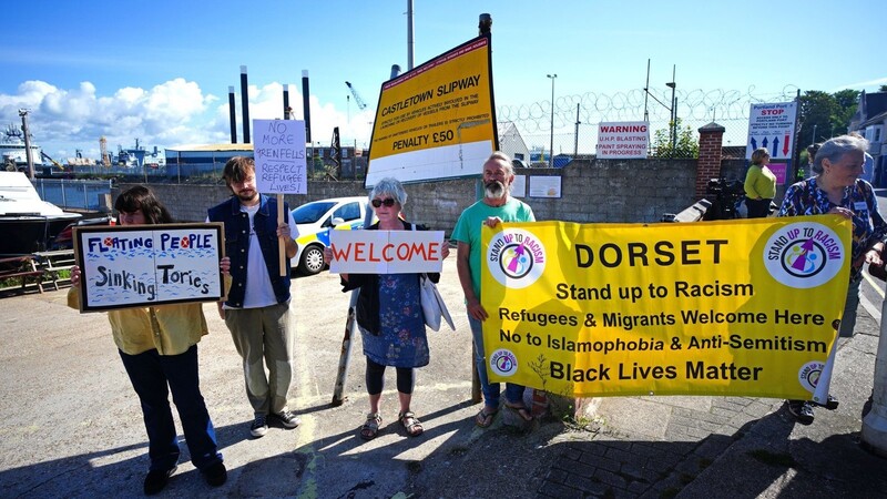Pro-Migrations-Demonstranten halten Fahnen und Plakate, während sie in der Nähe des Unterkunftsschiffes "Bibby Stockholm" im Hafen von Portland stehen. Zuletzt führten die Konservativen in England radikale Maßnahmen ein, um einen Rückgang der Migration zu forcieren.