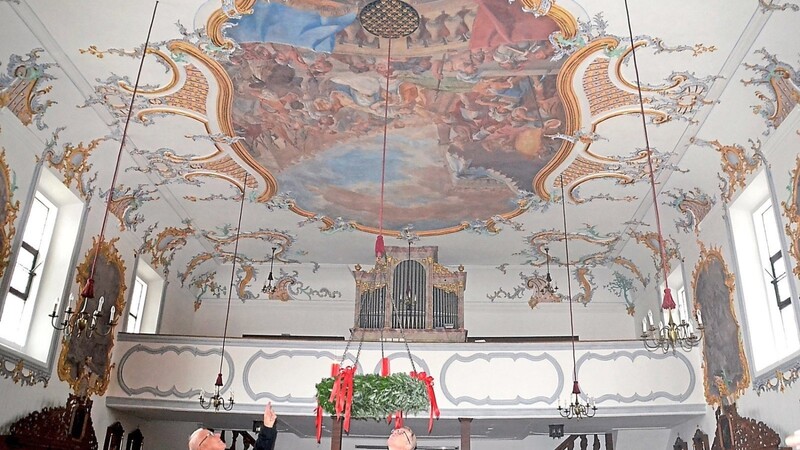 Mesner Josef Ehrenreich und Pfarrer Klaus Beck zeigen auf den vergitterten Lüftungsschacht, aus dem das Regenwasser ins untere Kirchenschiff lief. Ebenfalls zu sehen ist das restaurierte Deckengemälde.