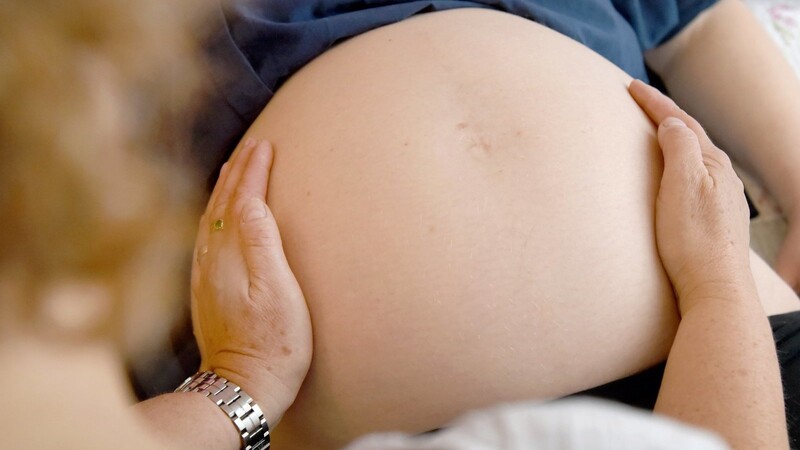 Eine Hebamme tastet den Bauch einer Frau ab, die im neunten Monat schwanger ist. In Niederbayern waren im Jahr 2022 laut einer Statistik rund drei Prozent weniger Hebammen verfügbar als im Jahr 2019.
