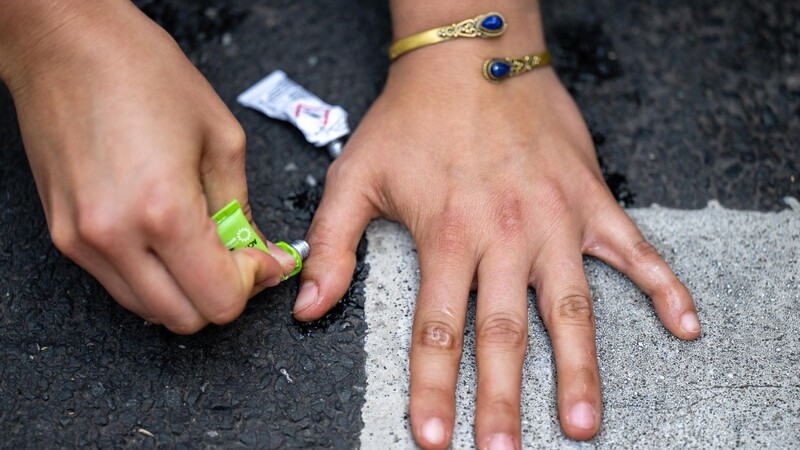 Die Hand einer Klimaaktivistin der Gruppe "Letzte Generation" klebt auf einer Straße. (Symbolbild)