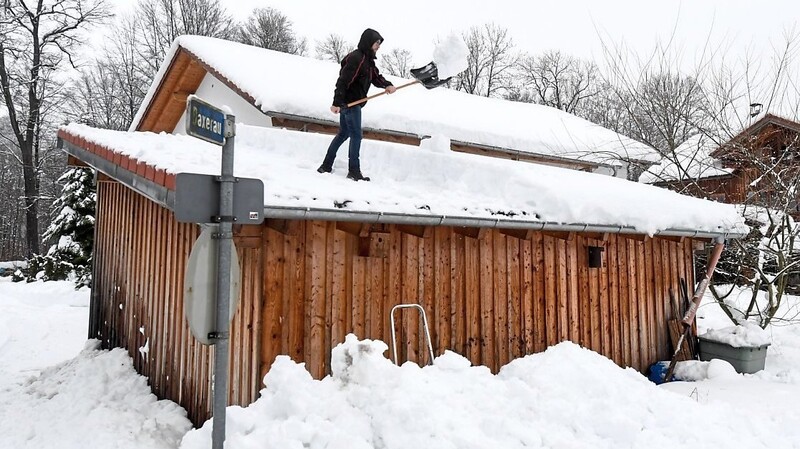 Ein Mann befreit in Traunstein das Dach eines Anbaus von den Schneemassen.