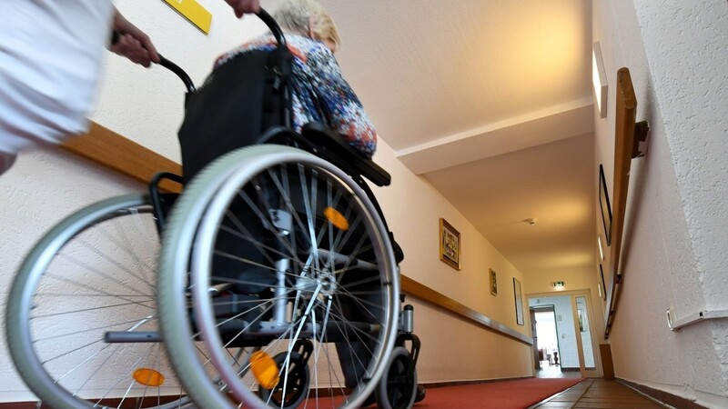 Eine Pflegerin schiebt eine ältere Dame im Rollstuhl über einen Flur in einem Seniorenpflegeheim.