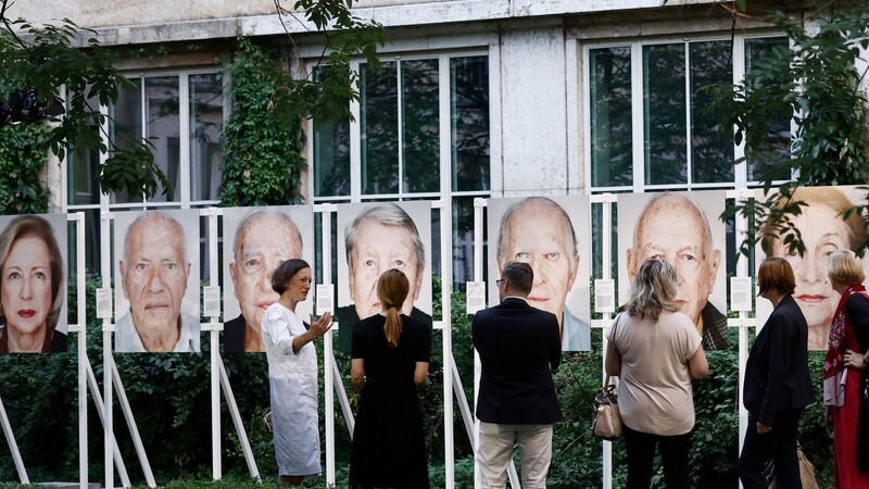 Gäste stehen vor Bildern der Ausstellung "Survivors. Faces of Life after the Holocaust" des Fotografen Martin Schoeller im Innenhof des Bundesministeriums für Finanzen.