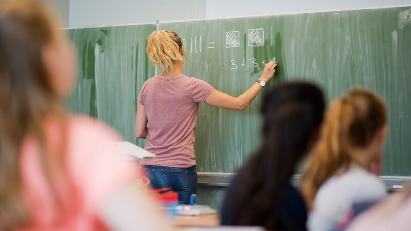 Eine junge Lehrerin schreibt im Mathematikunterricht an eine Schultafel.