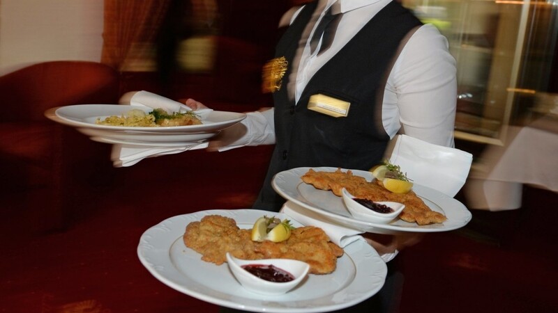 Eine Bedienung serviert in einem Restaurant Teller mit Schnitzeln und Braten. Ab 1. Januar soll der Mehrwertsteuersatz auf Speisen im Lokal von sieben auf 19 Prozent angehoben werden.