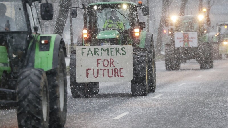 Traktoren fahren bei Schneefall bei einer Demonstration von Bauern über eine Straße.