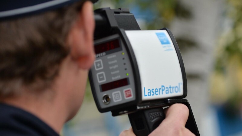 Ein Polizeibeamter misst mit einem Lasermessgerät die Geschwindigkeit eines vorbeifahrenden Autos.
