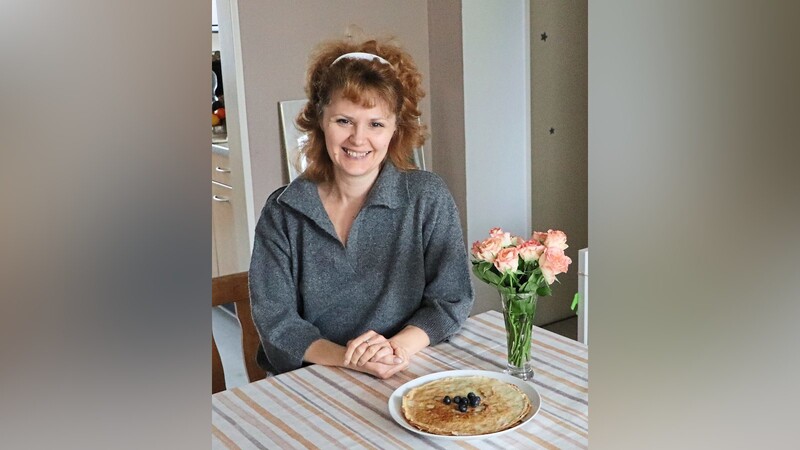 Am Esstisch in ihrer Wohnung sitzt Olena Kibalchich. Bliny mit Sahne und Zucker hat sie für alle gemacht - ein Rezept von Zuhause, das in ihrer Familie über Generationen weitergegeben wurde.
