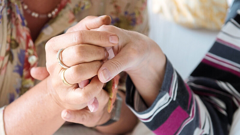 Eine Therapeutin in einem Hospiz hält die Hand einer todkranken Bewohnerin.