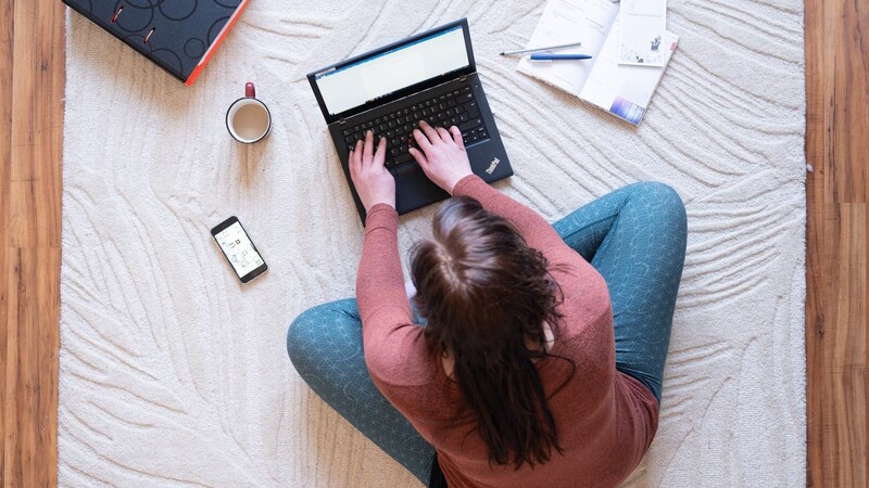 Eine Frau sitzt im Homeoffice auf einem Teppich und arbeitet an einem Laptop.