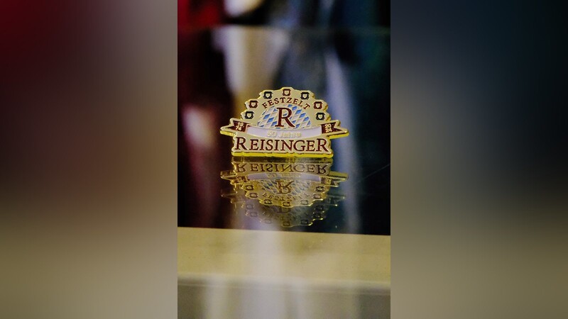 Der Jubiläums-Pin mit dem Reisinger-Logo, das von Riesenradgondeln umrahmt wird.