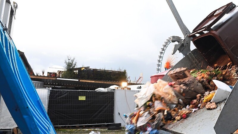 Eine Mülltonne wird am Rande der Theresienwiese vor dem Riesenrad mit einer Maschine in einen Müllcontainer ausgeleert.