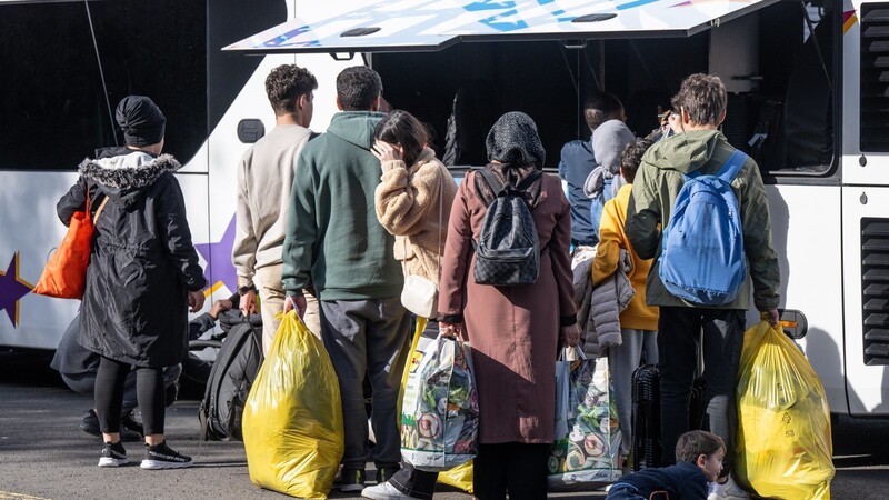 Flüchtlinge gehen zu einem wartenden Bus. Die Migration überfordert die Kommunen mehr und mehr.