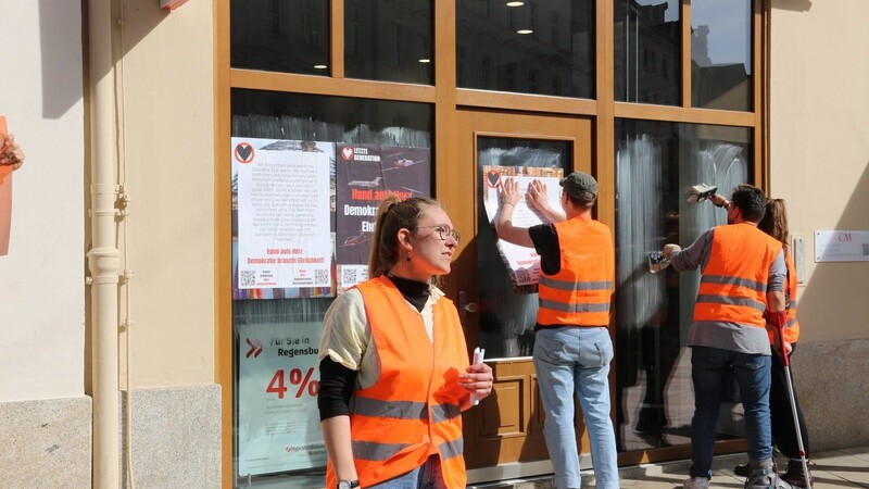 Mitglieder der Letzten Generation kleistern an eine Bankfiliale in der Altstadt ein Plakat.
