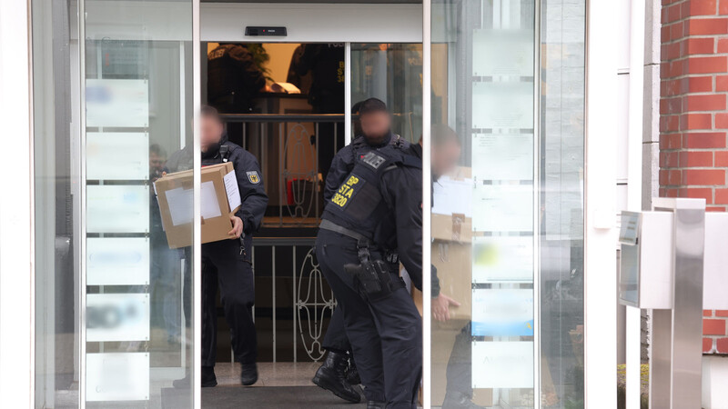 Polizeibeamte tragen in Solingen in Kartons sichergestelltes Material aus einem Gebäude.