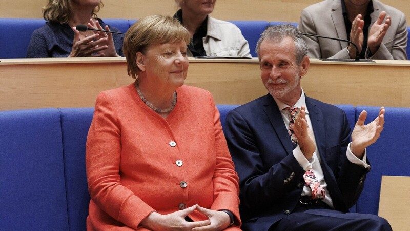 Altkanzlerin Angela Merkel sitzt neben dem Schauspieler Ulrich Matthes, der ihr für die Laudatio auf ihn hoch erfreut applaudiert.