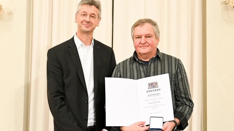 Kultusminister Piazolo (links) verleiht die Schulsport-Verdienstmedaille an Bernhard Weininger.