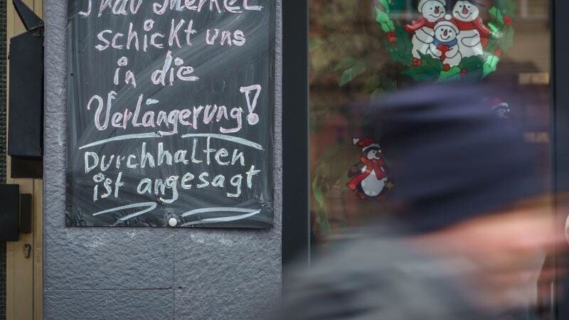 "Frau Merkel schickt uns in die Verlängerung! Durchhalten ist angesagt!" steht auf einer Tafel neben einem geschlossenen Geschäft im hessischen Friedberg.