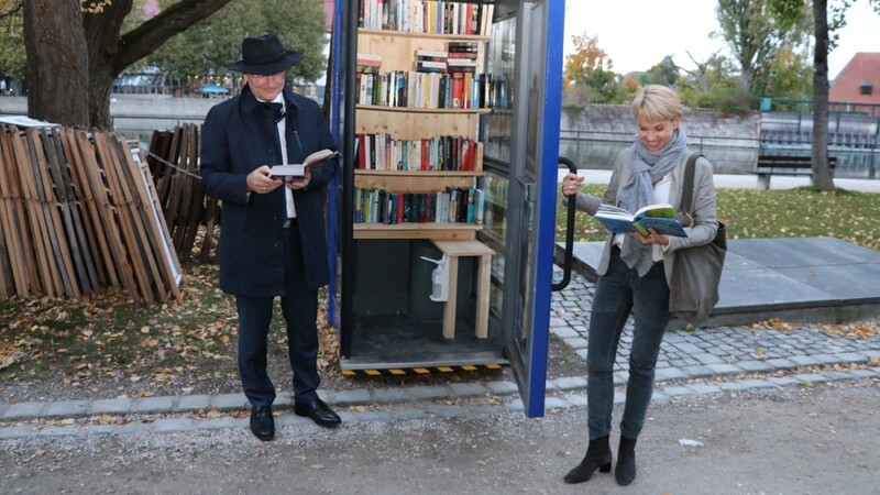 OB Alexander Putz und Peggy Füger, Präsidentin des Rotary Club Landshut/Trausnitz, machen eine Leseprobe bei der Einweihung der ersten Bücherzelle in Landshut.