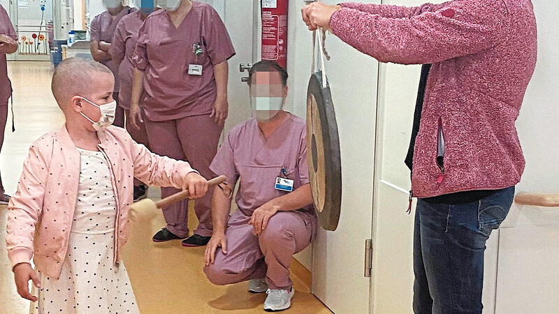 Mit drei kräftigen Gongschlägen beendet Sienna Rittler symbolisch ihre Intensivtherapie an der Kuno-Kinderuniklinik Regensburg. Mama Julia Rittler hält den Gong.