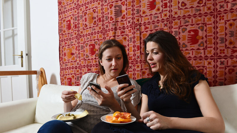 Zwei junge Frauen fotografieren mit ihren Smartphones in Berlin das Essen auf ihren Tellern.